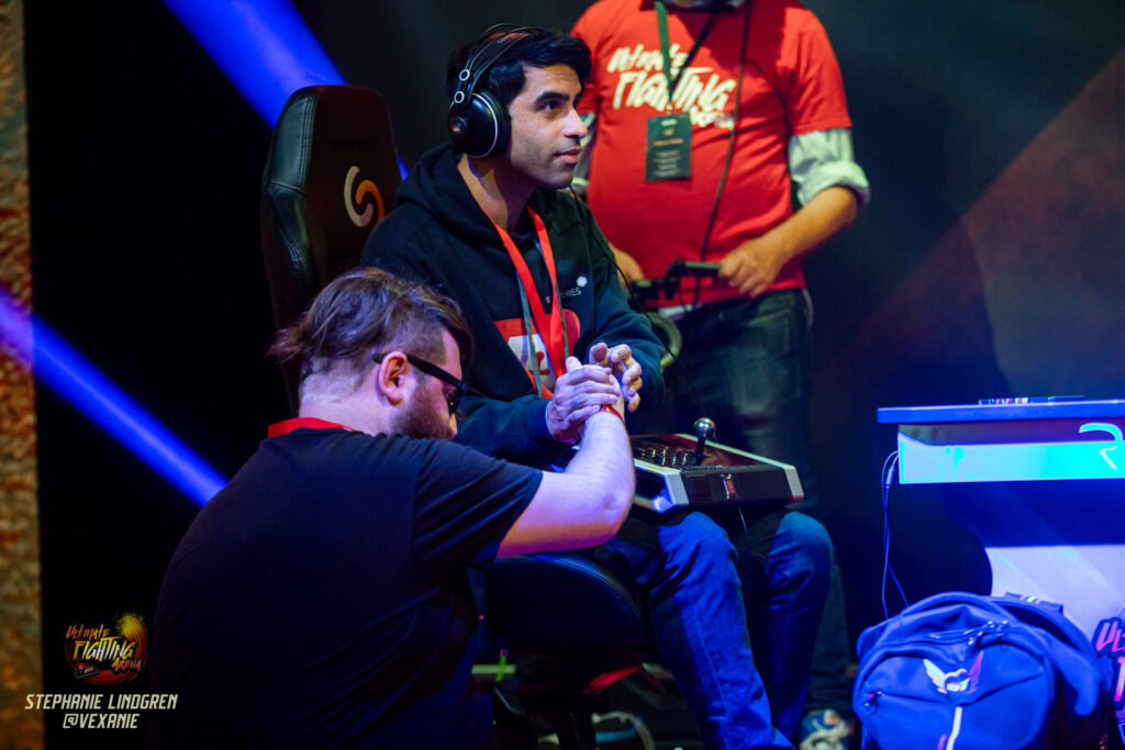 Boltstrike playing SFV on stage, while MQS grasps his hand.